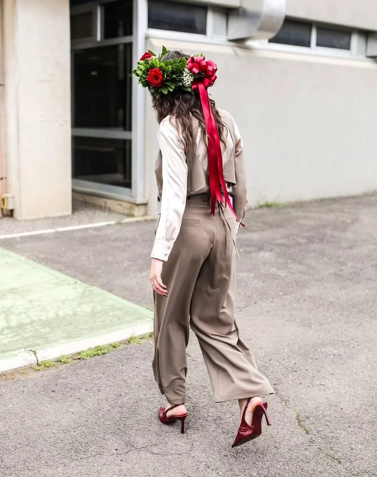 Ragazza cammina indossando una corona d'alloro con rose rosse e lungo nastro