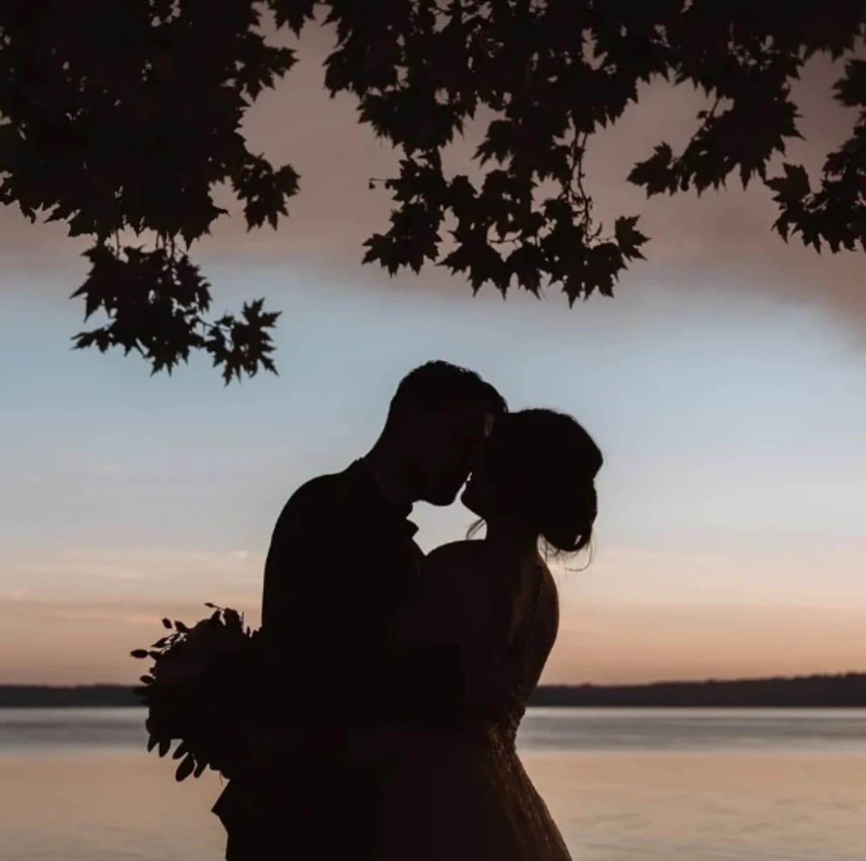 Sposi abbracciati al tramonto in riva al lago, la sposa con il bouquet